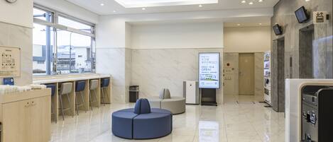 A modern hotel lobby with a reception desk, seating area, and a digital information board.