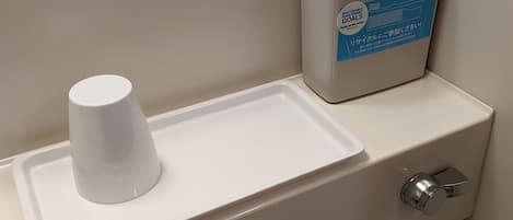 A bathroom sink with a cup holder and a trash bin.