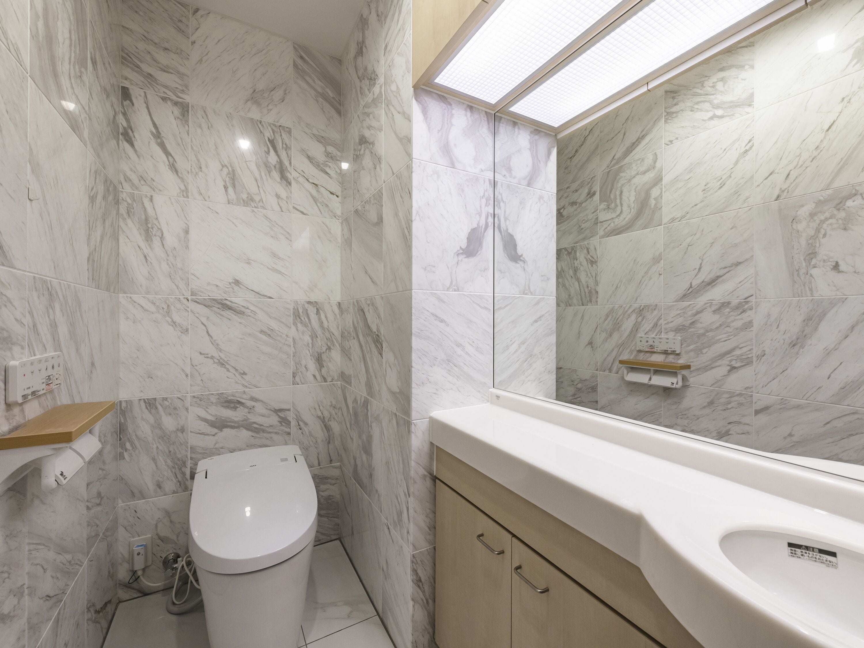 A bathroom with marble walls, a toilet, a sink, and a mirror.