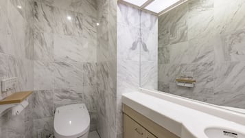 A bathroom with marble walls, a toilet, a sink, and a mirror.
