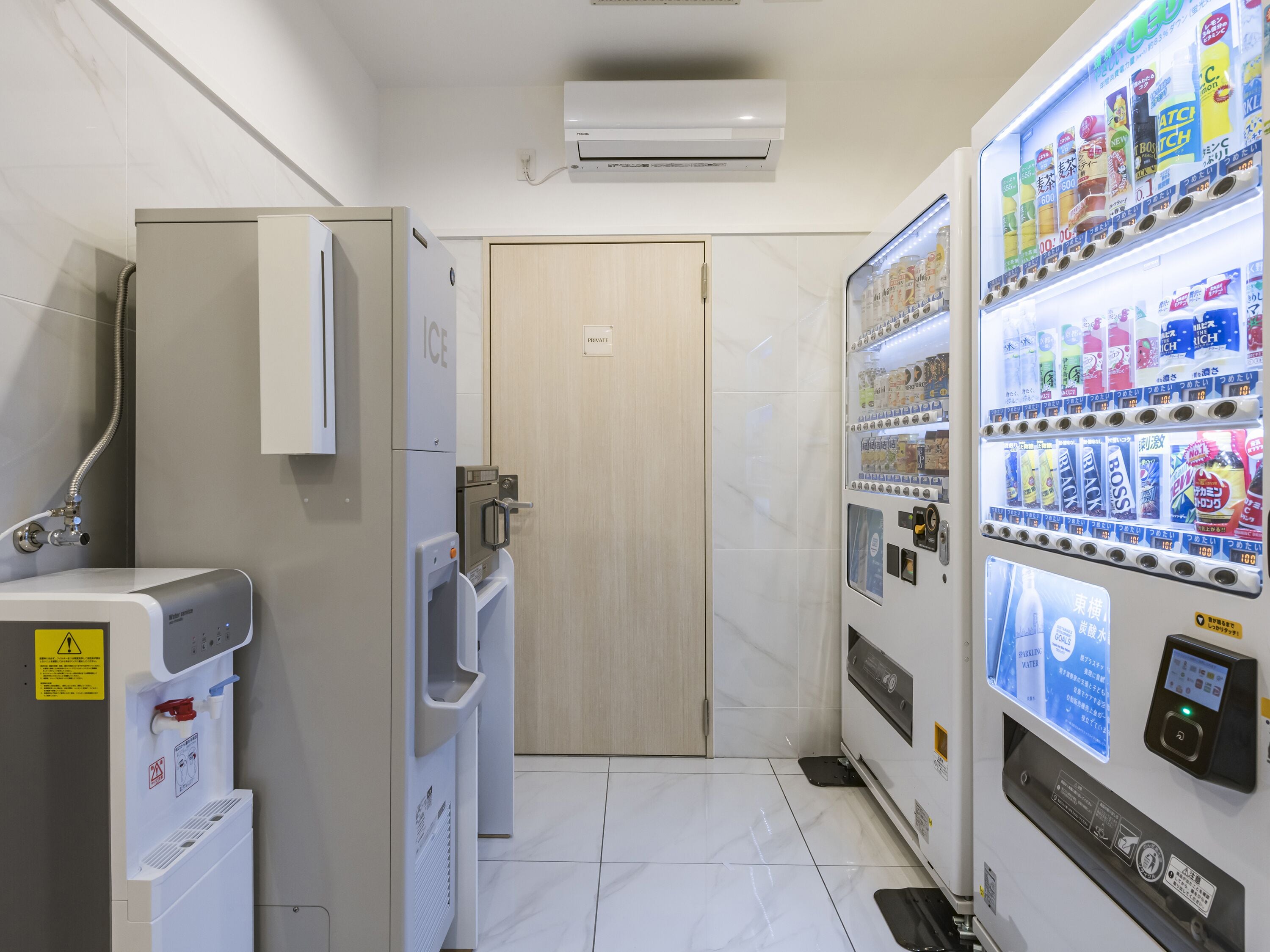 Un baño de hotel con ducha, puerta privada, dispensador de agua y máquina expendedora.