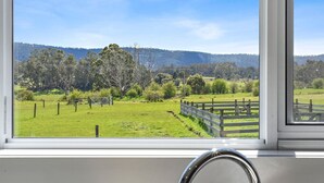 A window with a view of a green field, trees, and hills in the distance. - Wakefields - an enchanting mountain view cottage (Mole Creek)