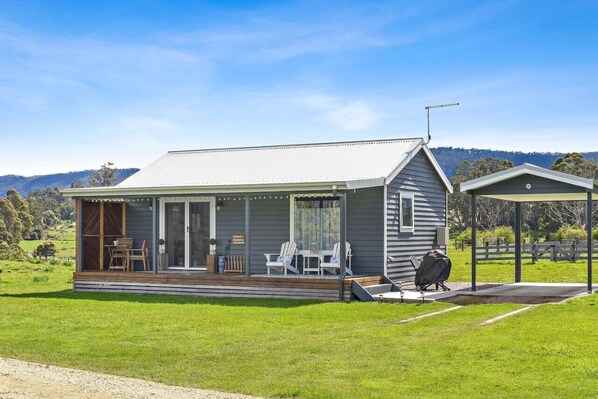 A single-story house with a covered porch, a barbecue area, and a view of the surrounding landscape. - Wakefields - an enchanting mountain view cottage (Mole Creek)