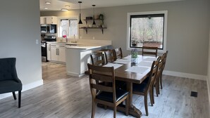 Una cocina moderna con una isla central, mesa de comedor de madera con sillas y un amplio ventanal con vistas a árboles.