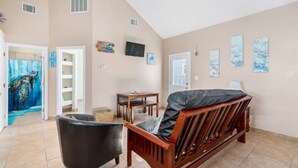 A spacious room with a wooden bed, a black armchair, a small table, and a television on the wall.