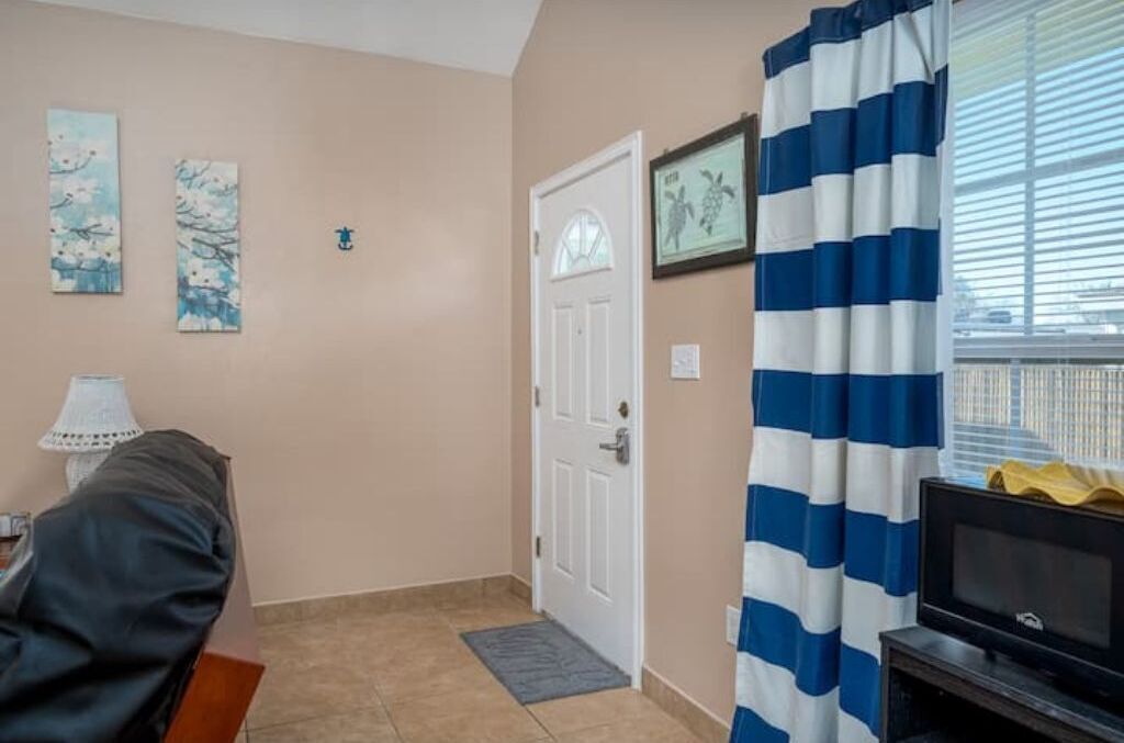 Une pièce avec une porte, un téléviseur, un rideau à rayures et deux tableaux accrochés au mur.
