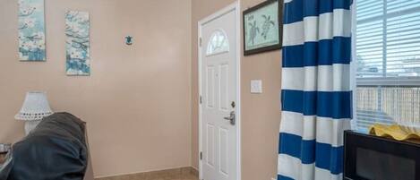 Une pièce avec une porte, un téléviseur, un rideau à rayures et deux tableaux accrochés au mur.