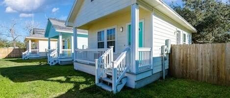 A row of two-story houses with a porch, wooden fence, and a grassy yard.