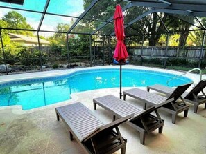 Una piscina con sillas de descanso y una sombrilla roja.