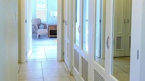 Ein Flur mit einer Tür zu einem Zimmer, das ein Bett und einen Sessel beherbergt. Schränke und ein Fenster mit Jalousien sind ebenfalls vorhanden.