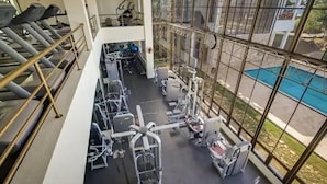 Ein Fitnessstudio mit Laufbändern, Krafttrainingsgeräten und einem Pool, die durch große Fenster sichtbar sind.