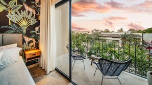 Un balcón con vistas a un paisaje urbano y una habitación con cama, mesita de noche y un mural.
