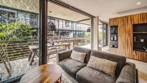 A modern living room with a sofa, a coffee table, and a view of an outdoor balcony. - Sublime 1BR w Cenote | Big Gym | Pools | Jacuzzis (Tulum)