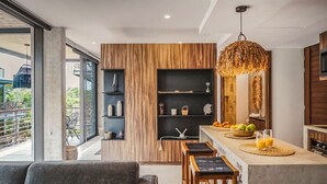A modern kitchen with a wooden accent wall, a hanging light fixture, and a breakfast bar with fruit and orange juice. - Sublime 1BR w Cenote | Big Gym | Pools | Jacuzzis (Tulum)