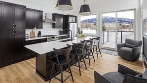 A modern kitchen with dark cabinetry, a central island, and bar stools. - Architectural Masterpiece Home with Mountain Views & Hot Tub (Red Lodge)