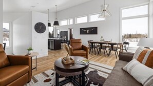 A spacious living room with a leather sofa, a round coffee table, and a dining area with a table and chairs. - Architectural Masterpiece Home with Mountain Views & Hot Tub (Red Lodge)