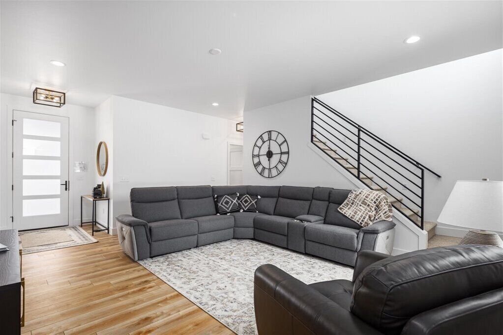 Ein modernes Wohnzimmer mit einem Ecksofa, einem kleinen Beistelltisch, einer Uhr und einer Treppe.