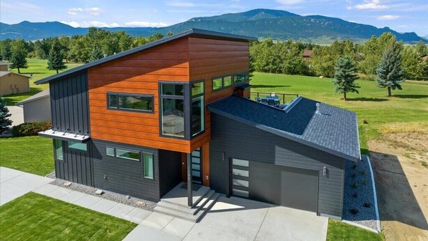 A modern two-story house with a garage, large windows, and a view of mountains. - Architectural Masterpiece Home with Mountain Views & Hot Tub (Red Lodge)