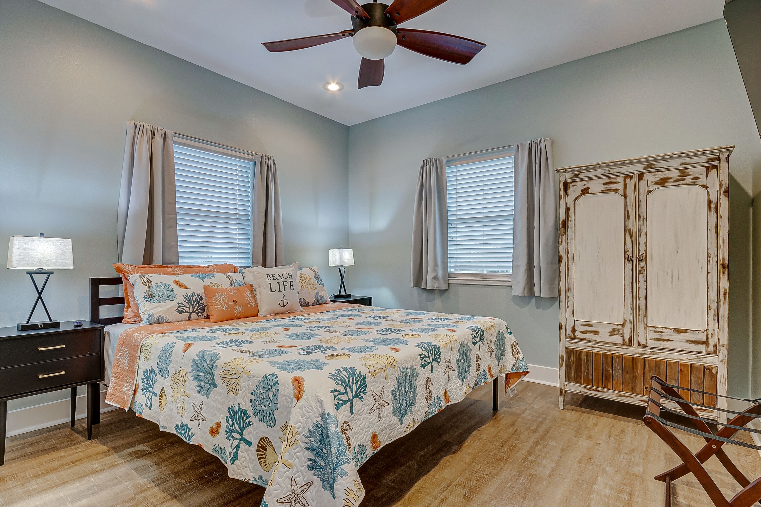 A bedroom with a bed, nightstands, a ceiling fan, and a wardrobe.