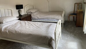 A bedroom with two single beds, a nightstand with a lamp, a wooden chair, and a small table with books. - A cosy retreat, ideal for walks and quiet relaxation. Pet friendly! (Brampton)