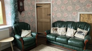 A room with a green leather sofa, a small round table, and floral wallpaper. - A cosy retreat, ideal for walks and quiet relaxation. Pet friendly! (Brampton)