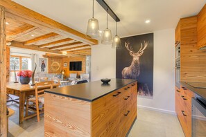 A modern kitchen with wooden cabinetry, a central island, pendant lighting, and a large deer poster on the wall. - Magnificent chalet 5 minutes from the center of Megève! (Megève)