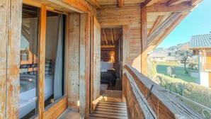 Varanda de madeira com piso e guarda-corpo de madeira, que dá acesso a um quarto com cama e janela.
