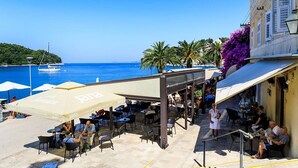 An outdoor café with tables and chairs, overlooking a body of water and a distant island. - Attractive House with A/C, Private Pool, Superb Views of the Konavle Valley, 5 mins walk to Gruda! (Gruda)