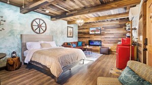 A cozy room with a wooden ceiling, a bed with a headboard, a red refrigerator, and a television on the wall.