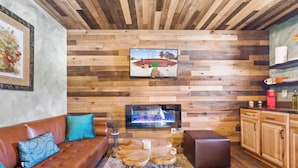 A cozy living room with a wooden wall, a flat-screen TV, a brown leather sofa, and a coffee table.