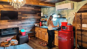 A kitchen with wooden walls, a chandelier, a red Galanz refrigerator, and a person cooking.