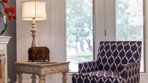 Een kamer met een gestreept fauteuil, een lamp op een bijzettafeltje en een raam met jaloezieën.