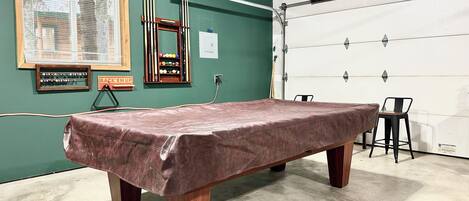 A pool table in a room with a green wall, a wooden frame, and a pool cue rack.