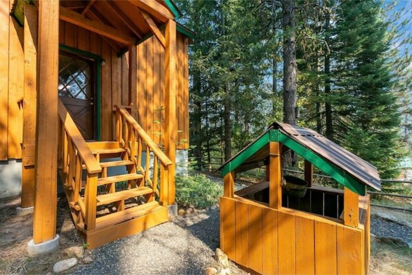 Situated in a wooded area, this cabin features a porch with a staircase and a separate storage structure.