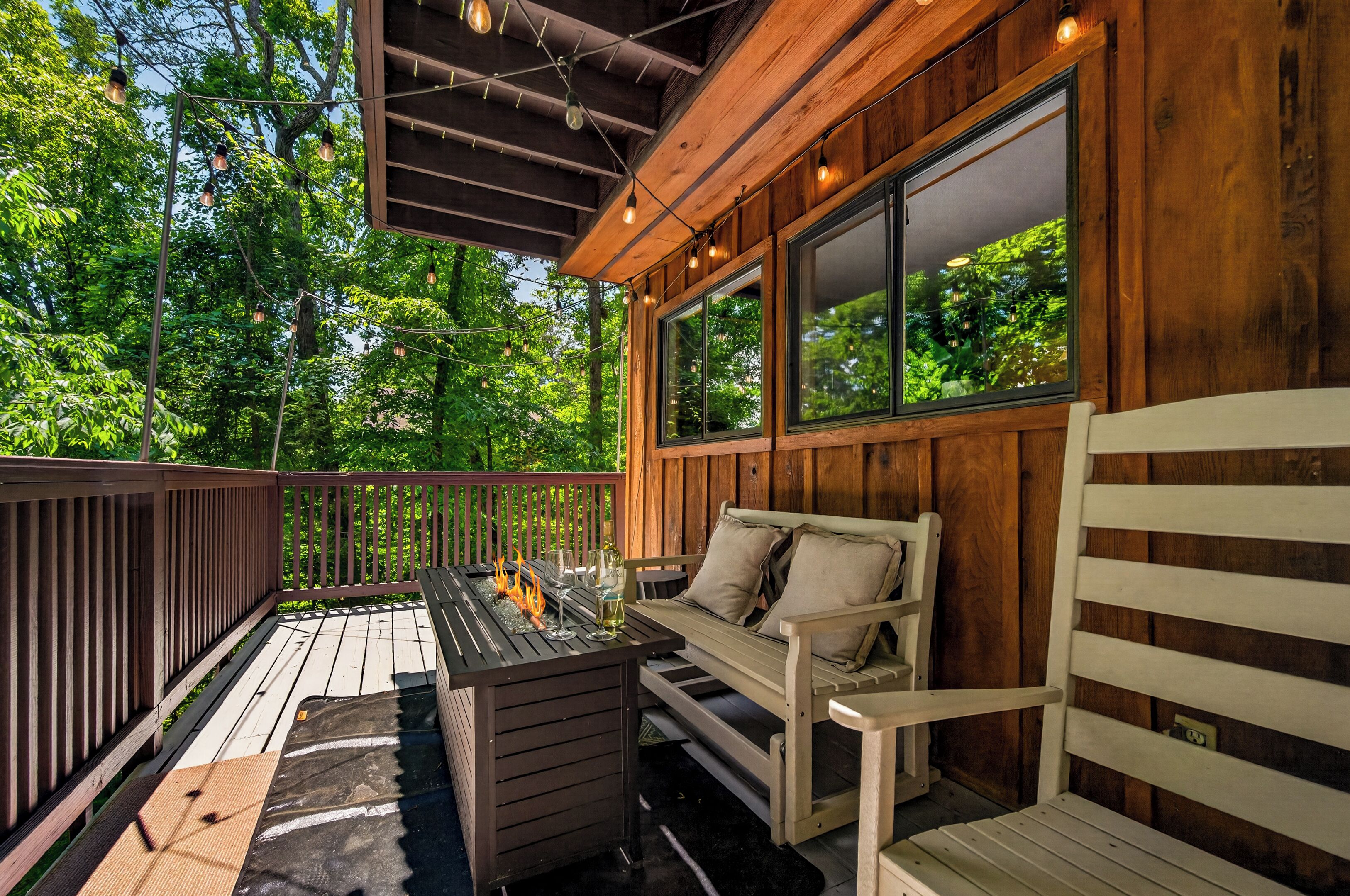 An outdoor deck with a fire pit, seating, and large windows overlooking a forest.