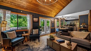 A spacious living room with a high ceiling, large windows, and a kitchen area. - Luxe Cabin, Dollywood, 4 min to Pkwy, Pups Welcome (Pigeon Forge)