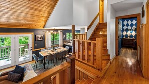 A wooden interior with a dining area, staircase, and a view of greenery outside. - Luxe Cabin, Dollywood, 4 min to Pkwy, Pups Welcome (Pigeon Forge)