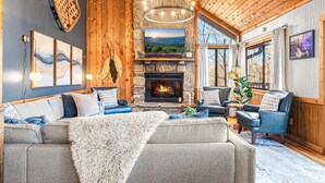 A cozy living room with a stone fireplace, comfortable seating, and a large window offering a scenic view. - Luxe Cabin, Dollywood, 4 min to Pkwy, Pups Welcome (Pigeon Forge)