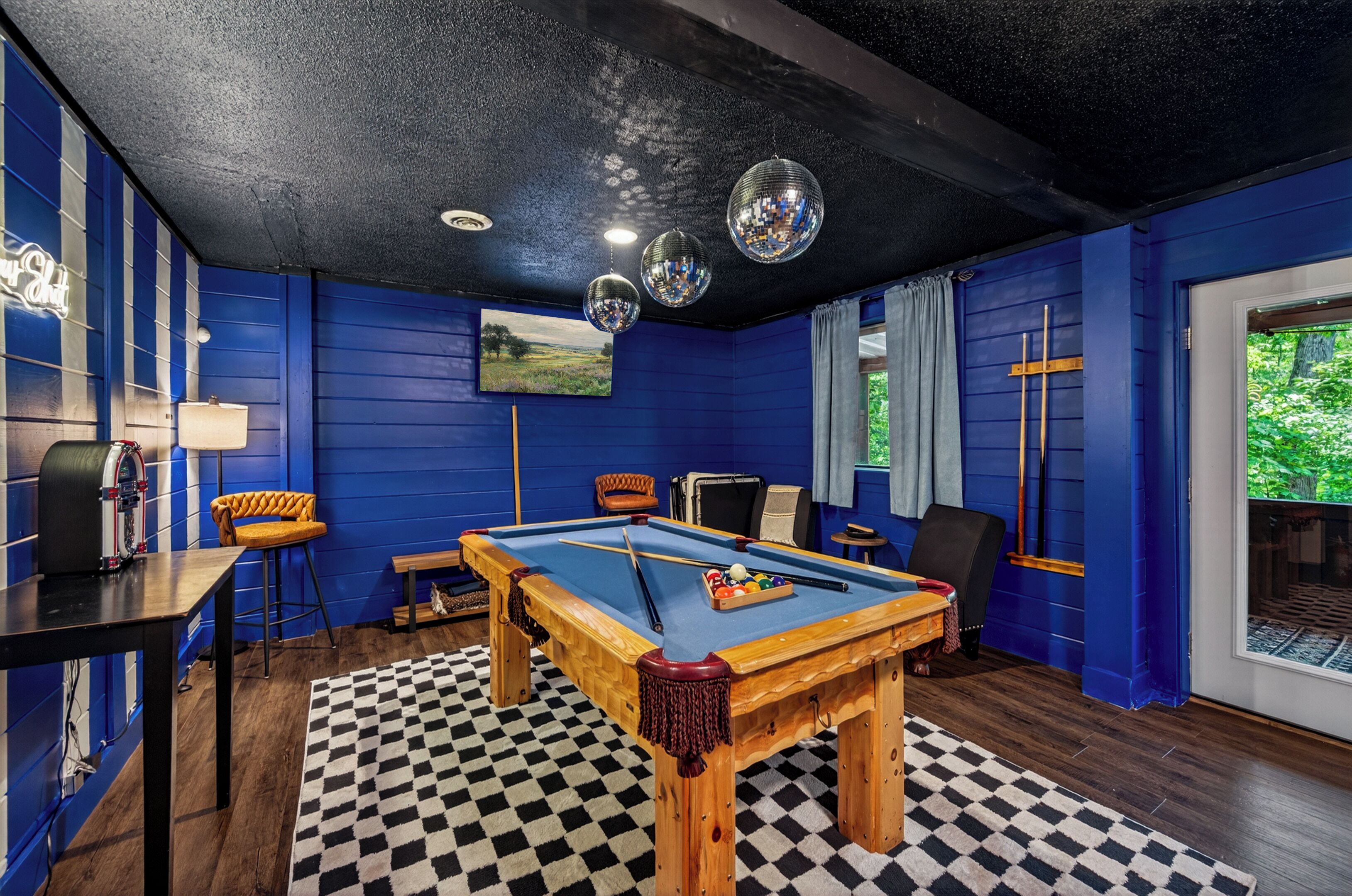 A pool table with billiard balls, a lamp, and a chair in a room with blue walls and a checkered floor.