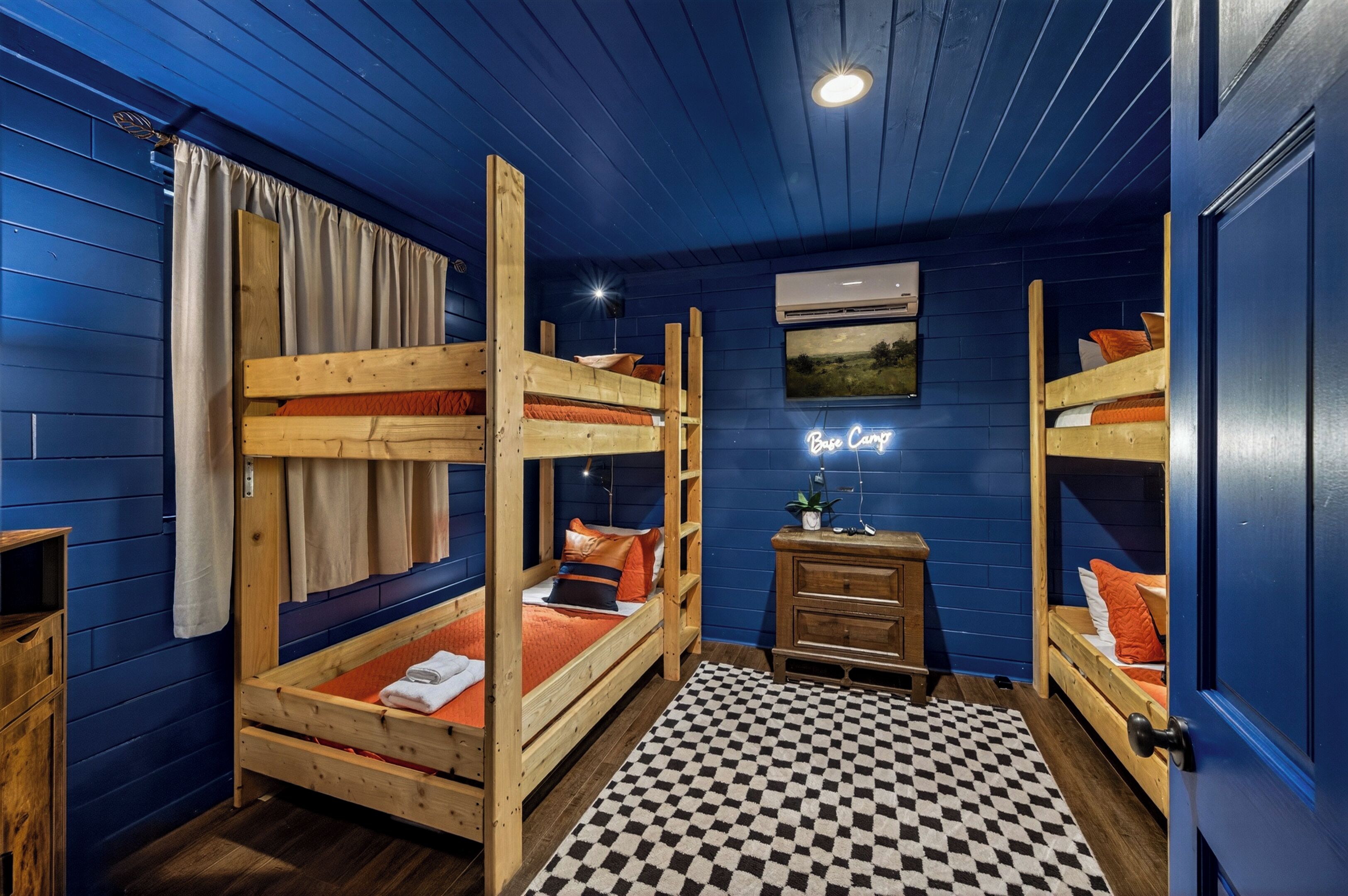 A room with bunk beds, a checkered rug, a wooden dresser, and a neon sign.