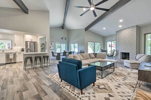 Relax in a spacious open-plan living area with a comfortable seating arrangement, sofa, and armchairs, complemented by a fireplace and large window with an outdoor view.