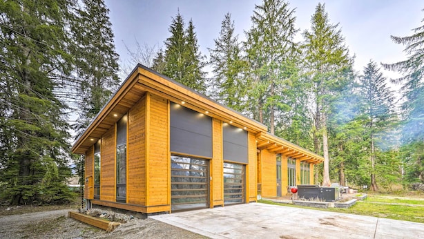 Een moderne houten chalet met grote garagedeuren, omgeven door dicht bos.