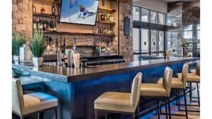 A bar area with a long counter, multiple stools, and a television screen. - Amazing One Bedroom suite w/sleeper sofa- Ski in/Ski out Grand Colorado Peak 8 (Breckenridge)