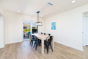 Un comedor con una mesa de madera y sillas negras, una lámpara colgante y una obra de arte enmarcada en la pared.