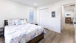A bedroom with a bed, a window with blinds, a door, and a hallway leading to another room. - Coastal Dream: New Heated Saltwater Pool/Hot Tub. Close to AMI, IMG, and LECOM. (Bradenton)