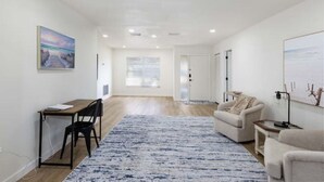 A modern living room with a wooden desk, a sofa, and a large rug. - Coastal Dream: New Heated Saltwater Pool/Hot Tub. Close to AMI, IMG, and LECOM. (Bradenton)