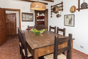 Ein Essbereich mit Holztisch, Stühlen, einer gewebten Pendelleuchte, einer Speisekammer mit Geschirr und einem gerahmten Bild an der Wand.