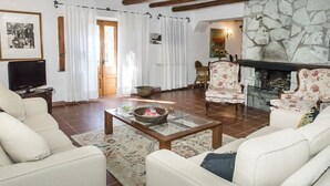 Un saló amb una llar de pedra, butaques florals, una televisió i una taula de centre.