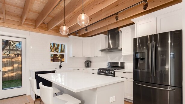Een moderne keuken met witte kasten, roestvrijstalen apparatuur en een centraal eiland met barstoelen.