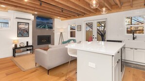 Een moderne keuken met witte kasten, een centraal eiland en een zithoek met een bank en een open haard.